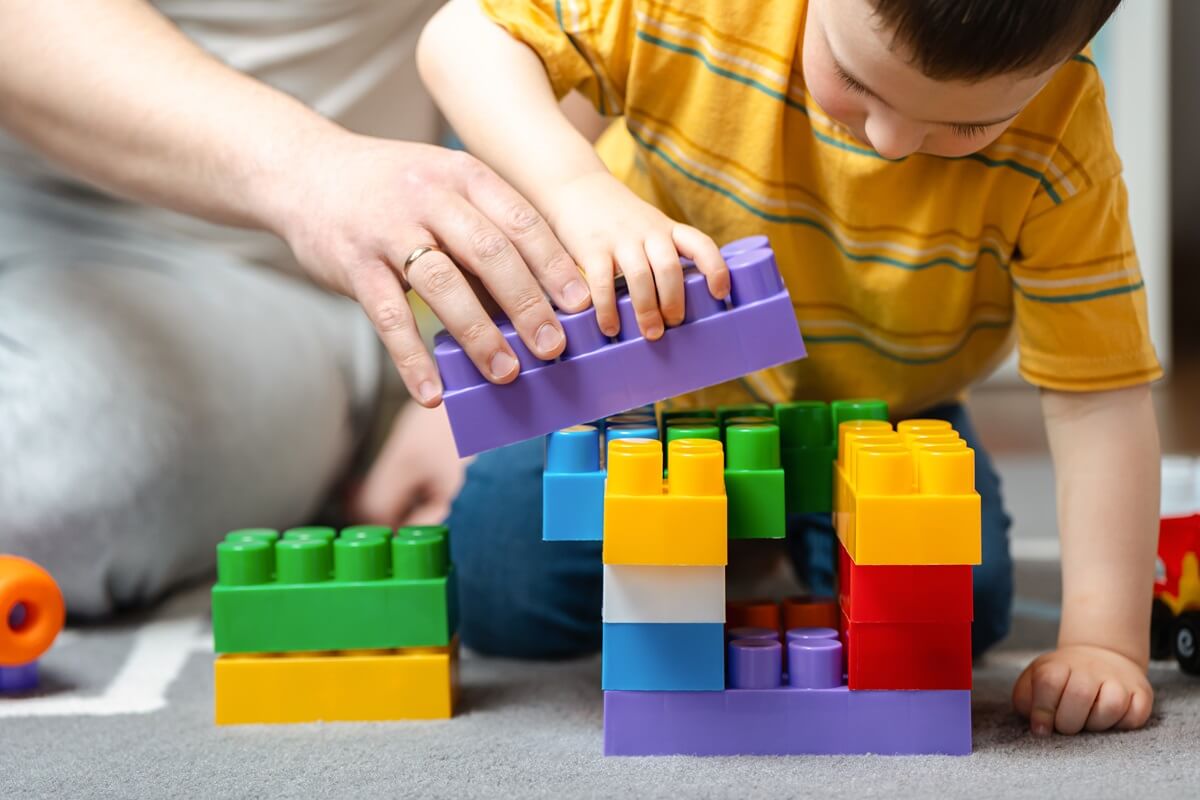 boy stacking big plastic colorful blocks while parent helps